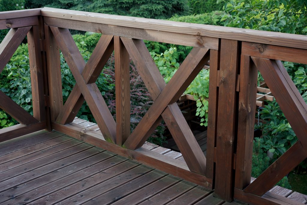 Balustrade avec balustres croisés en X, autour d’une terrasse en bois surplombant un jardin feuillu