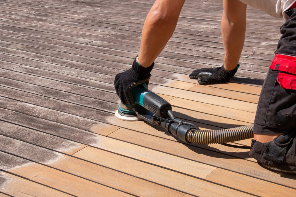 Ouvrier de la construction fait l’entretien d’une terrasse en ponçant la patine grise des planches de bois