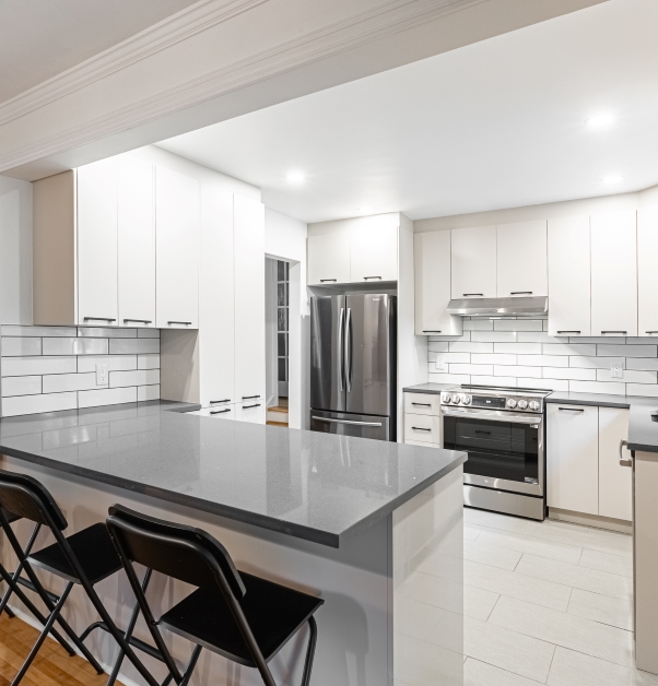 Classic white kitchen with view of white cupboards, white ceramic floor and gray stone peninsula.