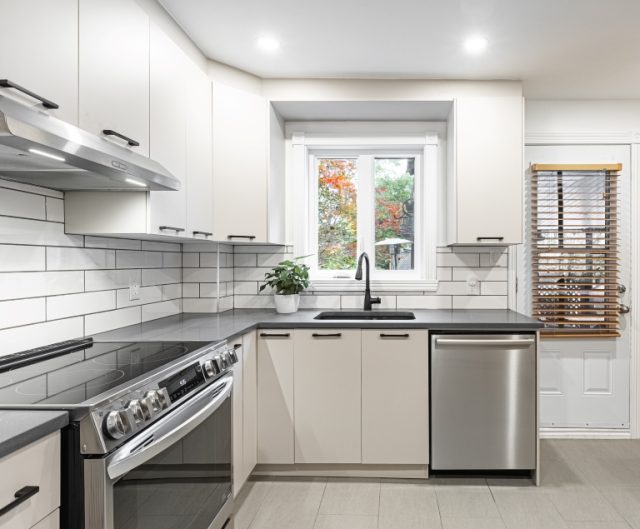 Cuisine classique blanche avec vue sur armoires blanches, dosseret de céramique blanche, fenêtre blanche, cuisinière et lave-vaisselle en acier inoxydable, porte d’entrée blanche et plancher de céramique blanche.