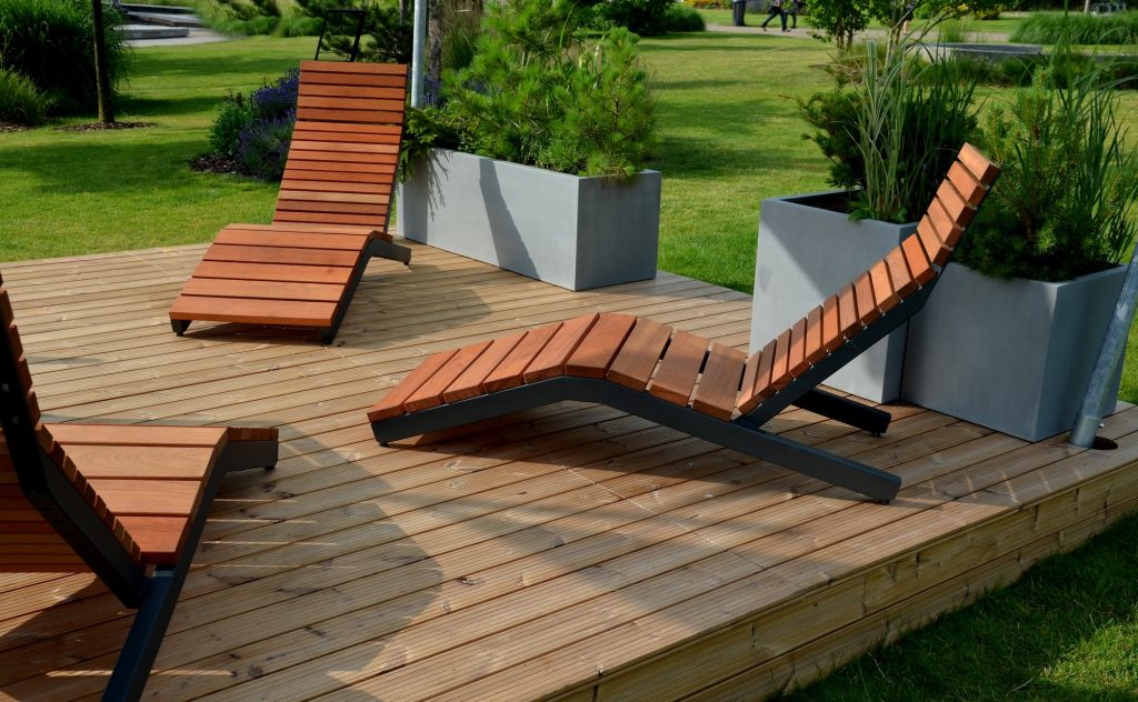 Patio en bois traité teinte naturelle avec trois chaises longues et arbustes en pots