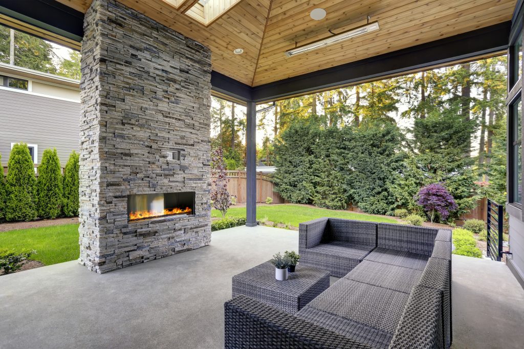 Terrasse en béton gris avec foyer de pierre grise, toit de bois teinte naturelle, mobilier gris et poutres métalliques grises