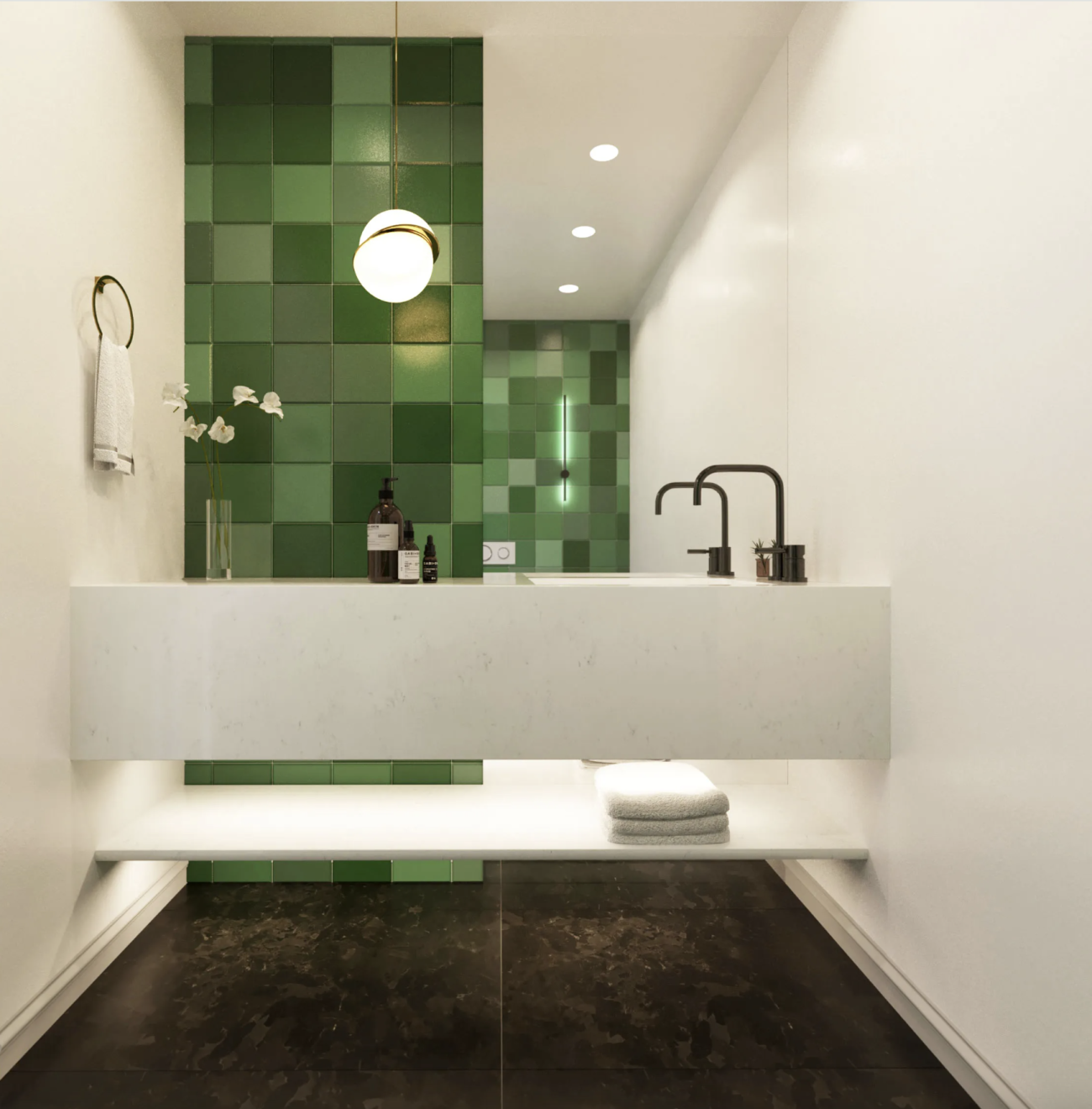 In a bathroom, a half-wall covered with zellige tiles in various shades of green, marble vanity, beauty products on the countertop, black fixtures, globe-shaped light fixture