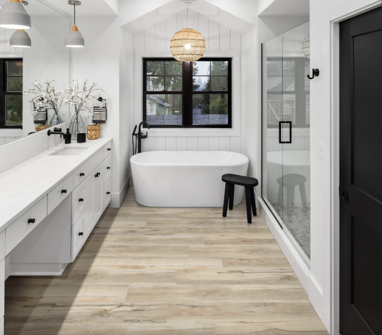 Bathroom blending farmhouse and Japanese styles, with an oval bathtub placed in a paneled alcove, bath stool, rattan globe pendant light, wood-imitating vinyl tiles, multi-drawer vanity unit, industrial lighting, and large shower with double glass doors