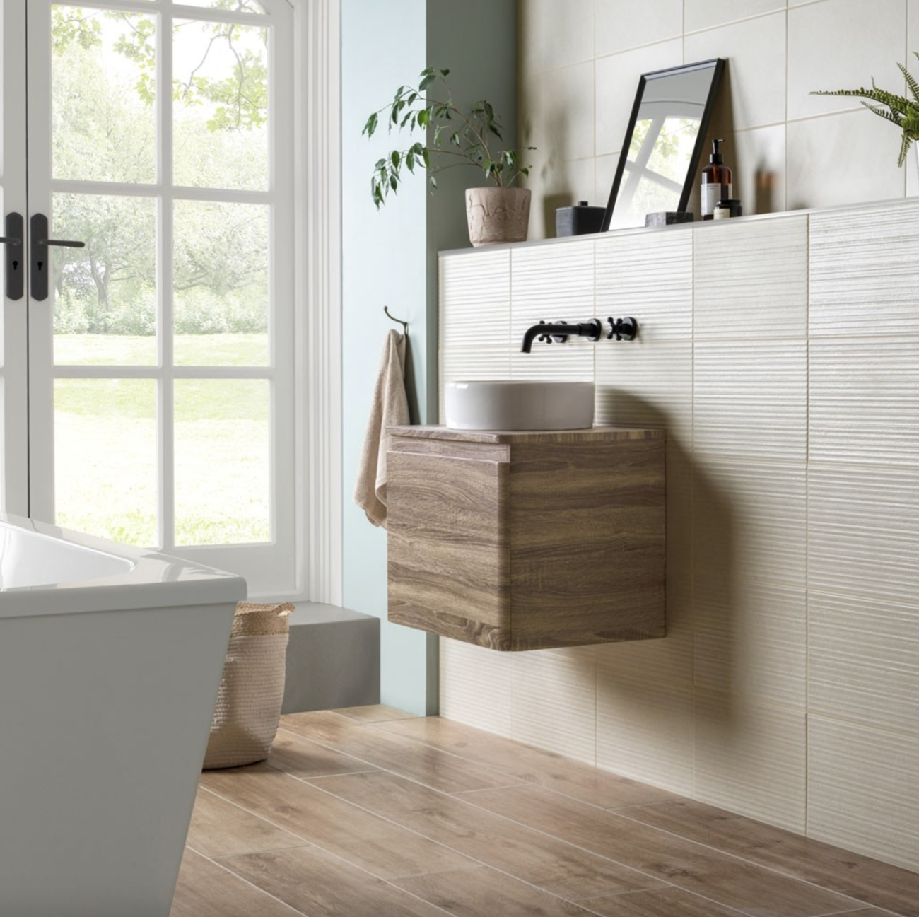 In a bright bathroom thanks to French doors, a full-height half-wall covered with grooved white tiles, topped with a floating wooden countertop and porcelain basin