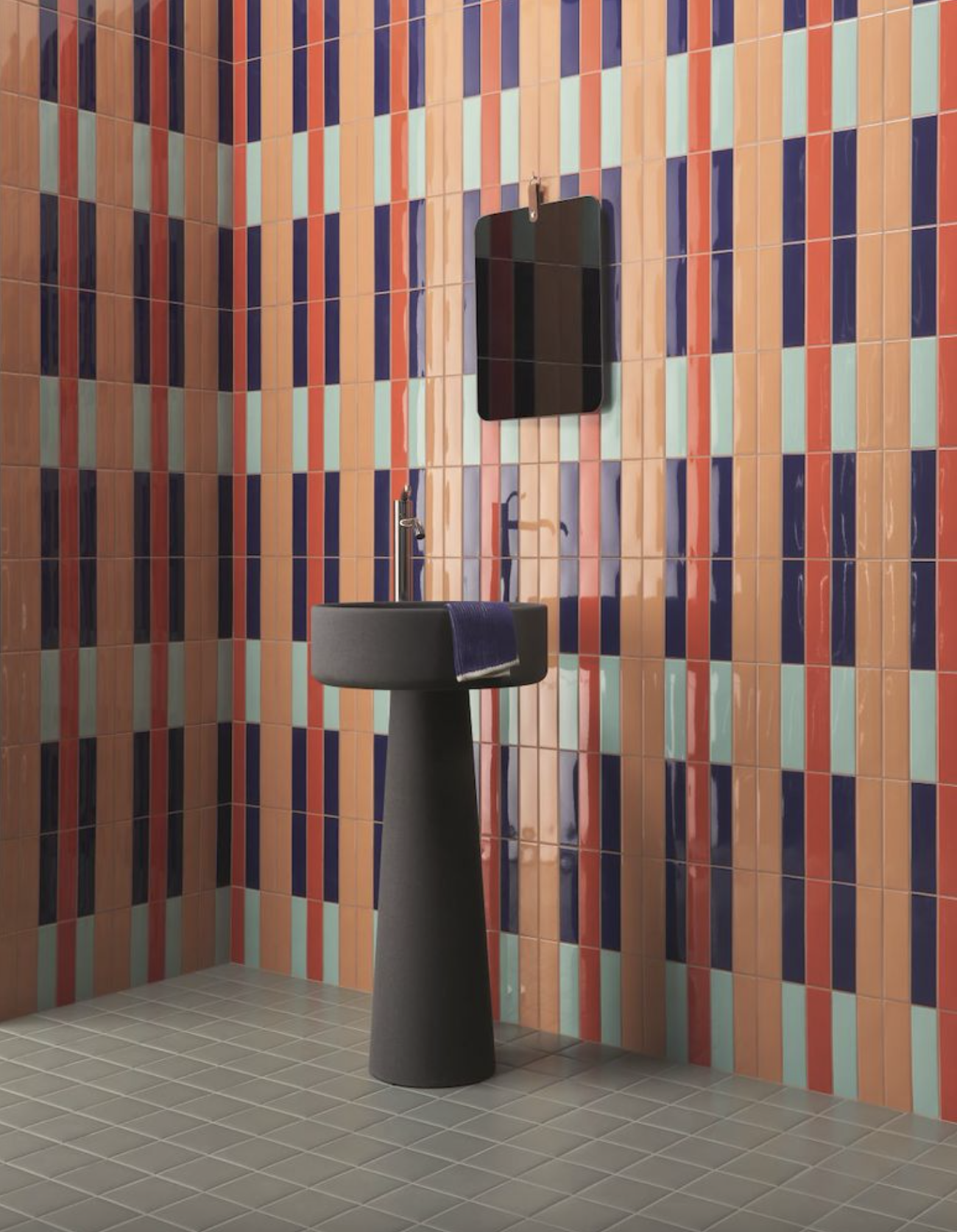 Bathroom with grey pedestal sink and wall decorated with vertically aligned multi-coloured rectangular tiles