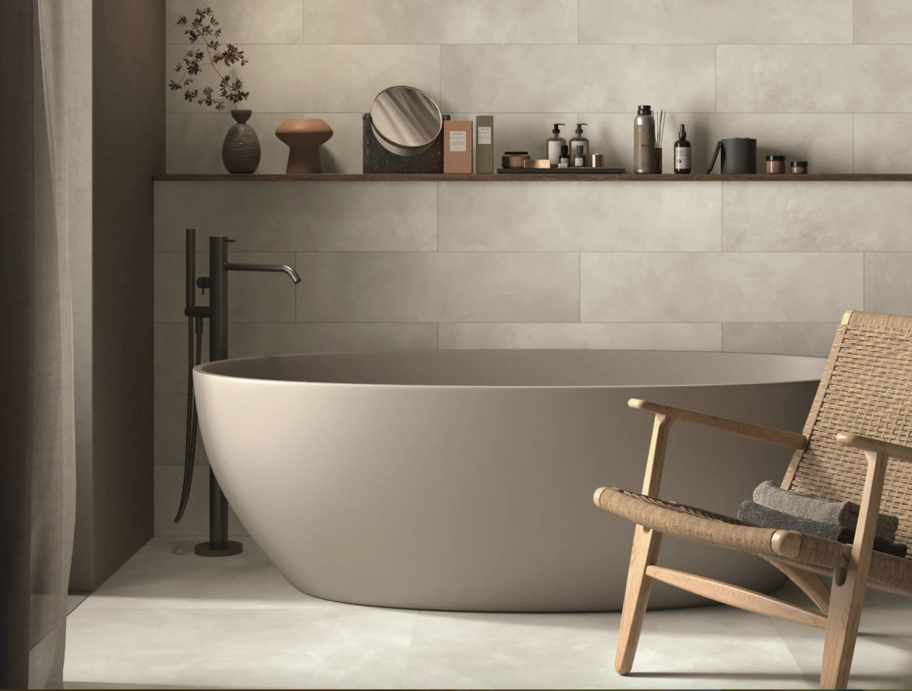 In a Japandi-style bathroom with taupe and brown shades, an oval bathtub, Hans J. Wegner chair, shelf with beauty products, wall and floor covered with slate tiles