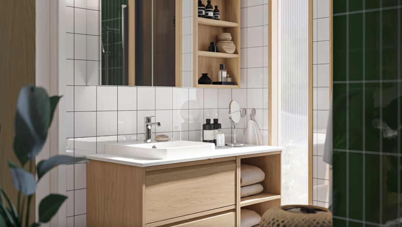 Bathroom with a wall of square white ceramic tiles and another covered with dark green rectangular tiles, pale wooden shelves and storage unit, white vessel sink, wicker basket