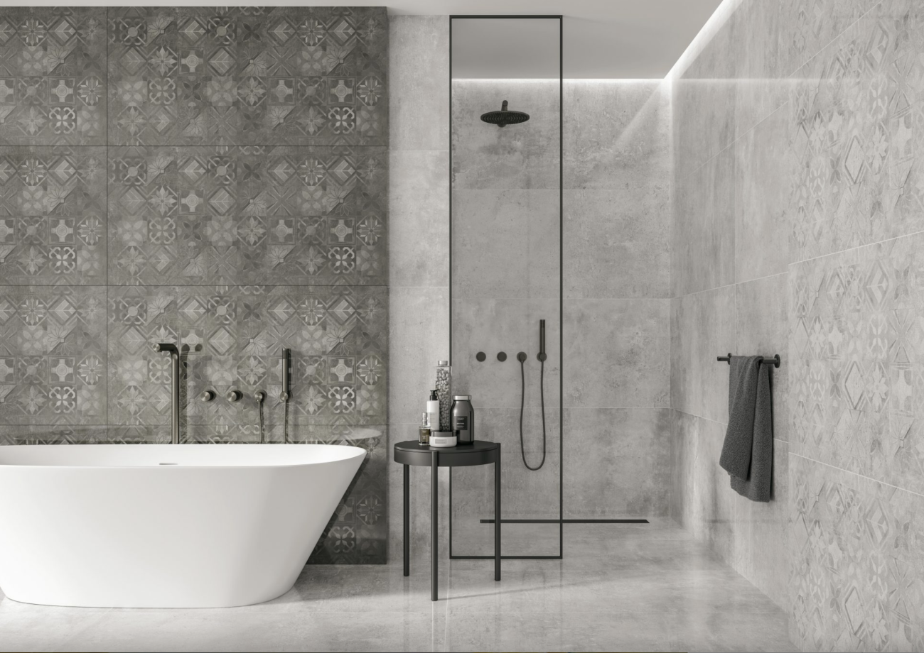 Salle de bain déclinée en nuances de gris, carrelages en ciment de style azulejos sur les murs et carreaux grand format à effet marbré dans la douche à l’italienne. Baignoire autoportante blanche et tabouret bas avec produits de beauté