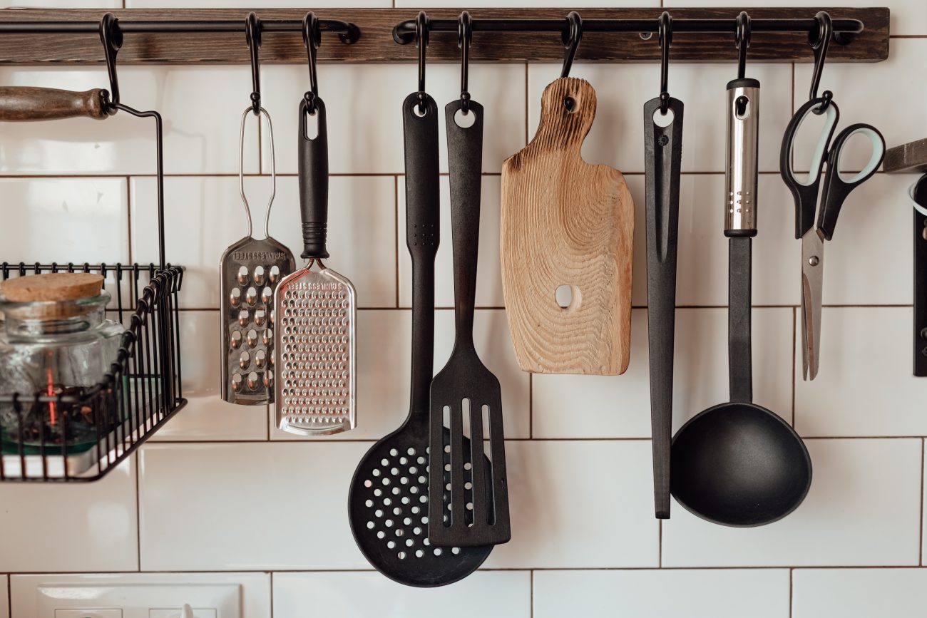 In a farmhouse-style kitchen, a white subway tile backsplash with a support holding graters, spoons, cutting board, and other kitchen utensils