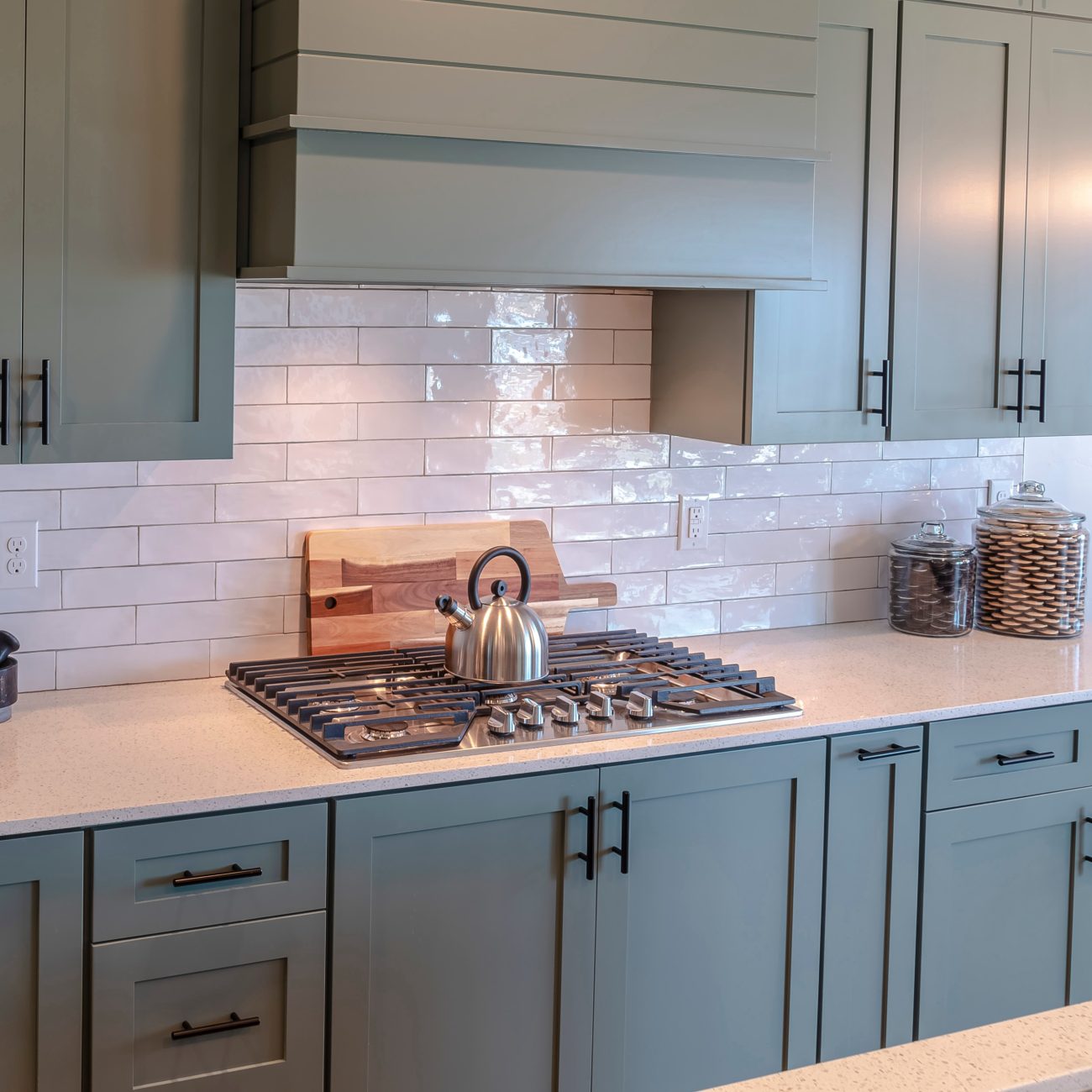 Farmhouse kitchen with dark grey cabinets, white glossy metro tiles backsplash and kettle on gas stove 