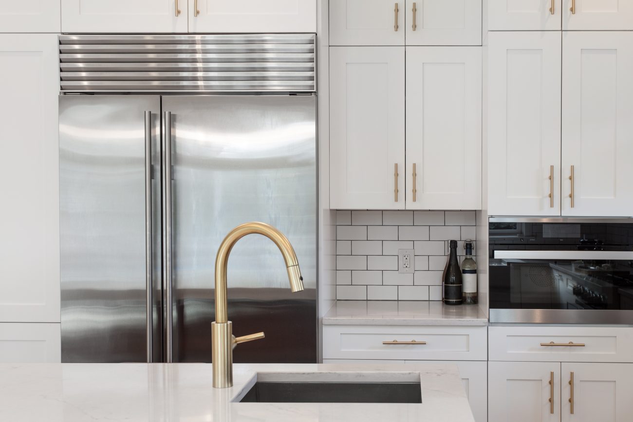 White kitchen built with Shaker cabinets, granite countertop, subway tile backsplash, stainless steel refrigerator, gold faucet and hardware