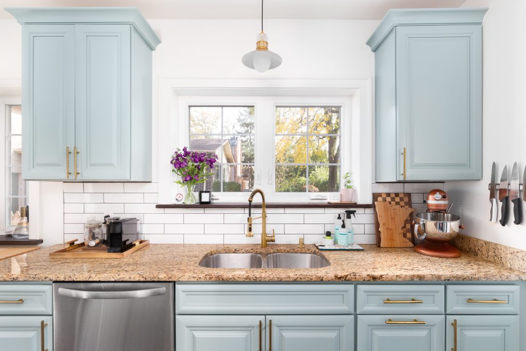 Farmhouse kitchen with sky blue cabinets and drawers, granite countertop, white subway tile backsplash and gold faucet