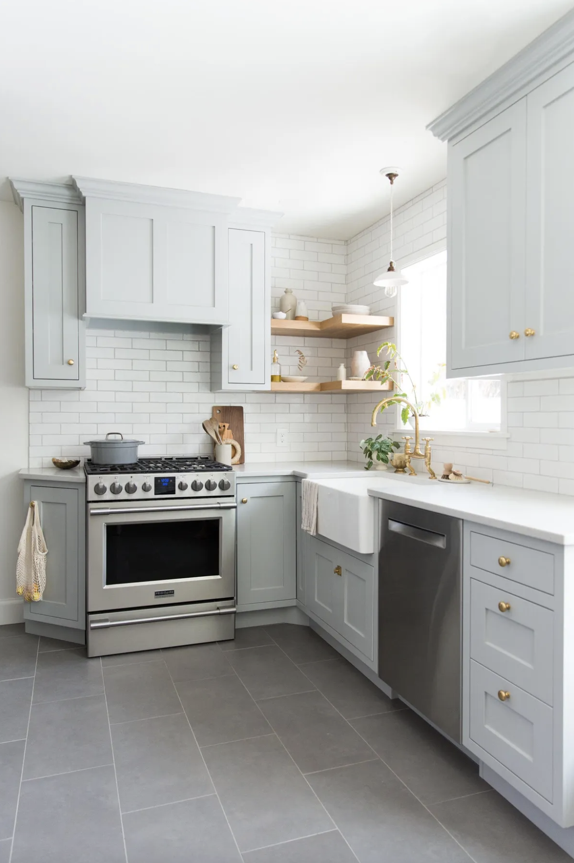 Farmhouse kitchen with grey cabinets, white metro tiles backsplash, wood corner shelves, apron front sink, gold faucet and doorknobs