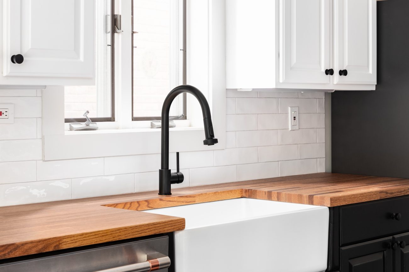 Black faucet detail with white cabinets, a butcher block countertop, and a white subway tile backsplash