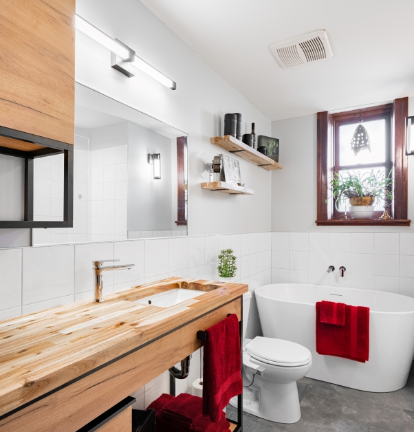 Side view, small, contemporary white bathroom with white ceramic wall tile, grey ceramic floor, natural-toned wood countertop, various accessories and red decorative touches