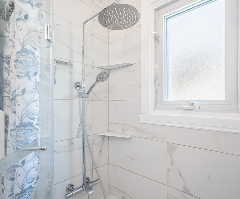 Salle de bain classique blanche avec vue sur douche de céramique blanche, robinetterie et fenêtre blanche