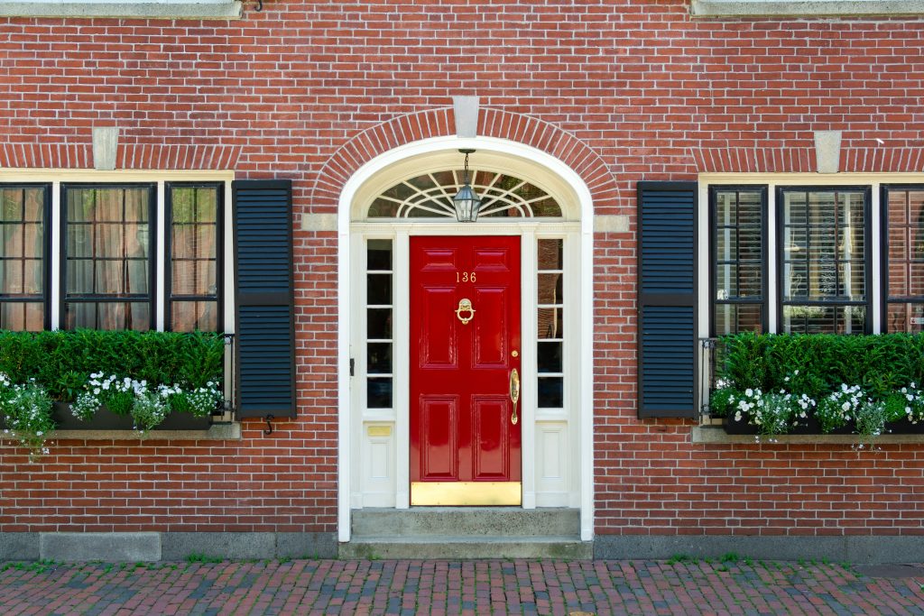 Une porte rouge avec des dorures décore la façade d’une maison de briques