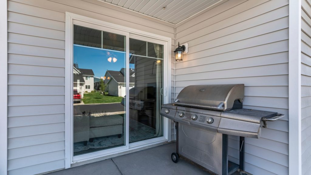 Une porte-patio vitrée donne accès à un balcon sur lequel se trouve un barbecue