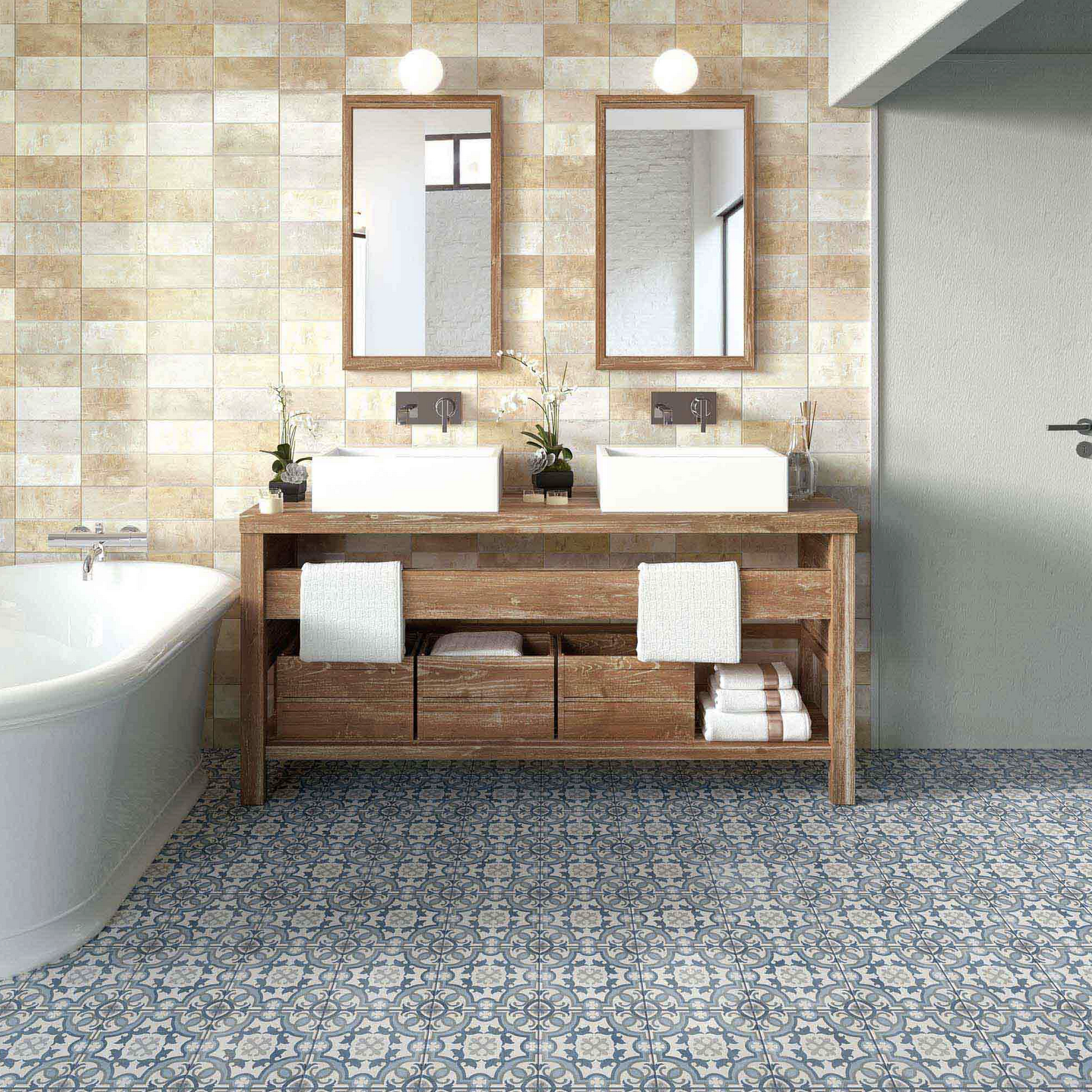 Blue rosette pattern cement tile floor, vintage wooden vanity with drawers and towel bar, two square vessel sinks on the countertop, limestone tile walls in various neutral shades, two vertical mirrors