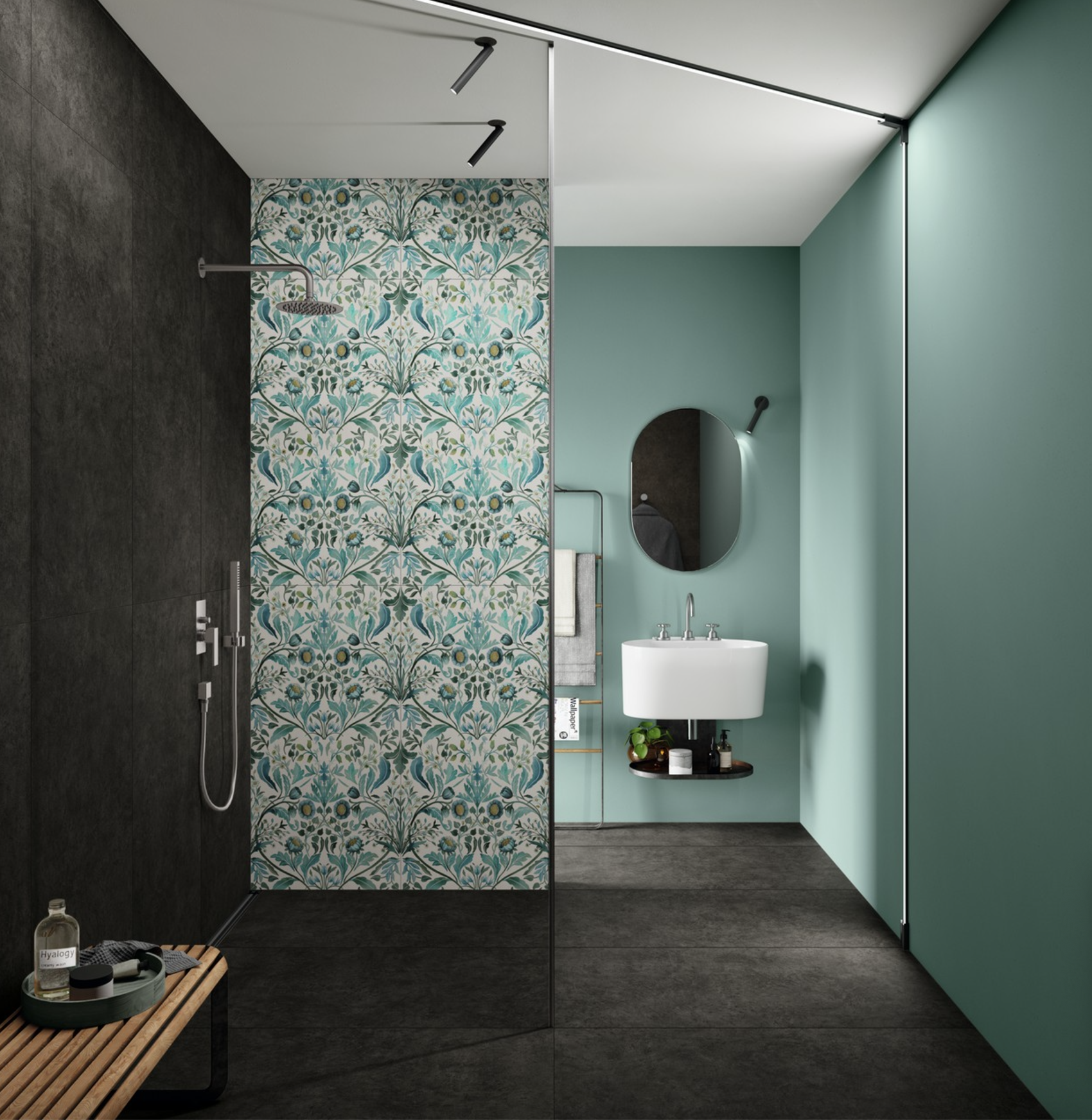 Revêtement en ardoise noire sur le plancher et un des murs de la douche italienne, mur de couleur turquoise orné d’un miroir ovale et d’un lavabo en porcelaine blanche sous lequel se trouve une étagère avec des produits de soins, tuiles à motifs floraux sur l’autre mur de la douche 