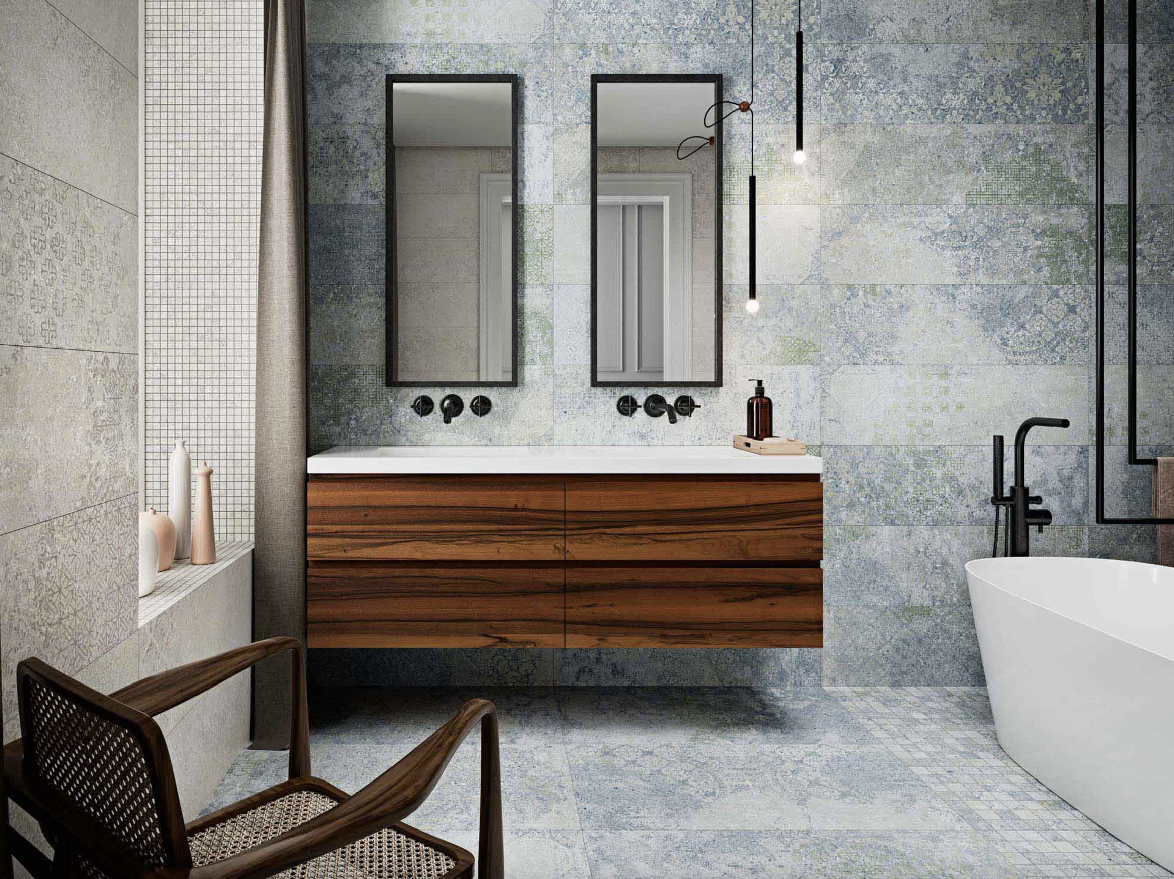 Salle de bain à mur et plancher recouverts de carreaux en ciment bleu et vert à motifs estompés, meuble-lavabo en bois foncé à deux lavabos sous plan, chaise en bois et cannage, deux miroirs verticaux, robinetterie noire, baignoire autoportante blanche 